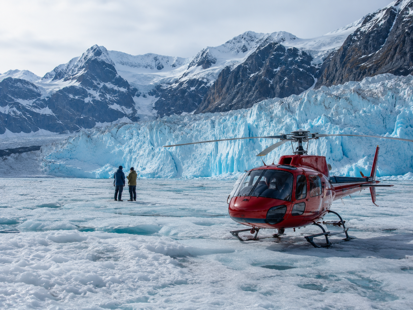 Couple standing beside a red helicopter on a glacier with snowy mountains behind