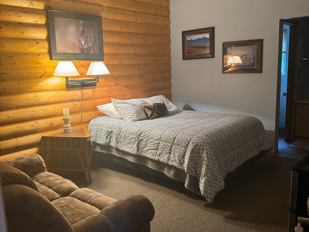 Queen room with warm log walls, queen bed, and reading chair